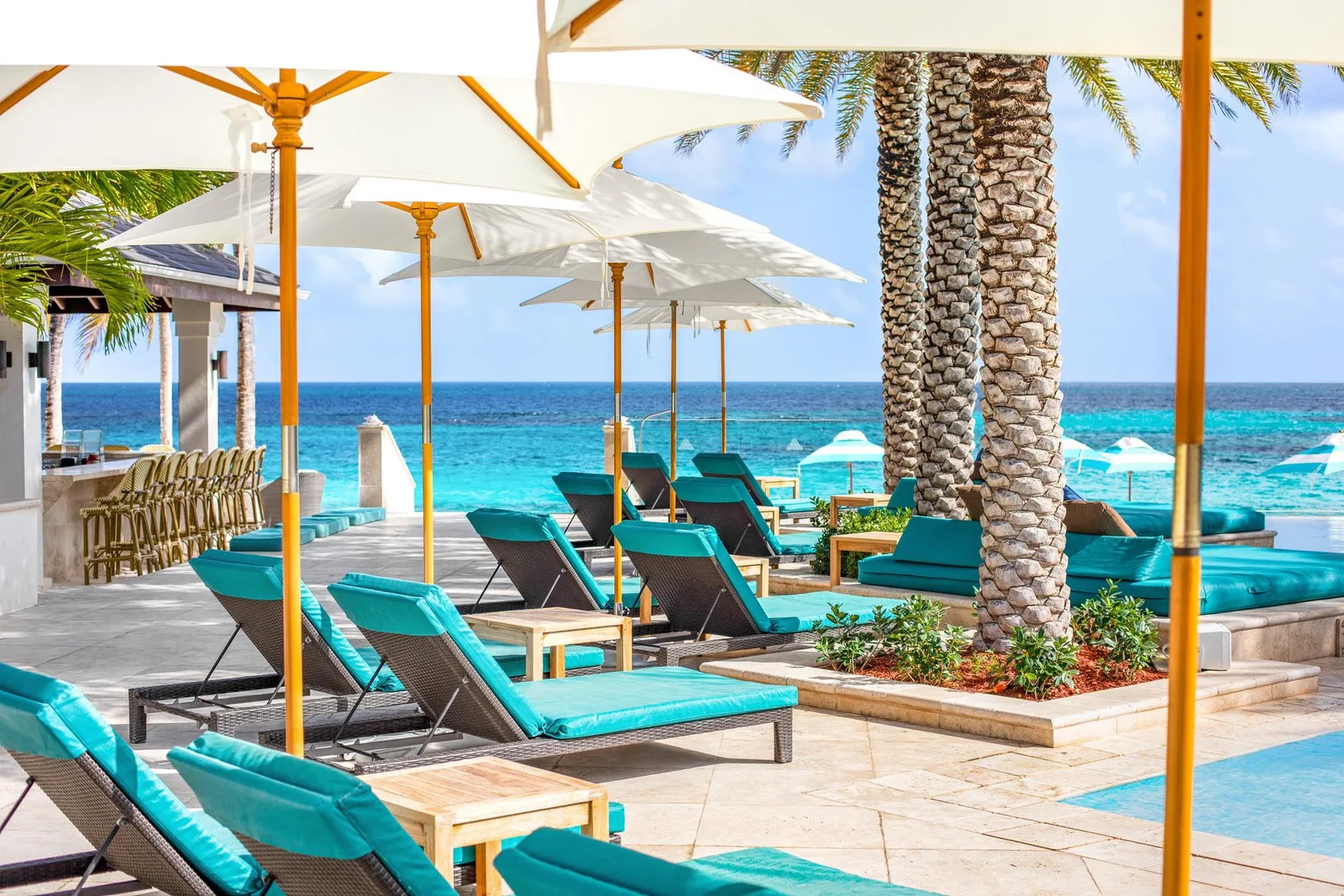 Turquoise lounge chairs sit beneath white sun umbrellas on a resort terrace overlooking the ocean in Anguilla.